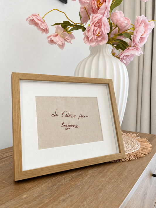 Burgundy embroidered French handwriting displayed in a wooden frame. Frame not included.